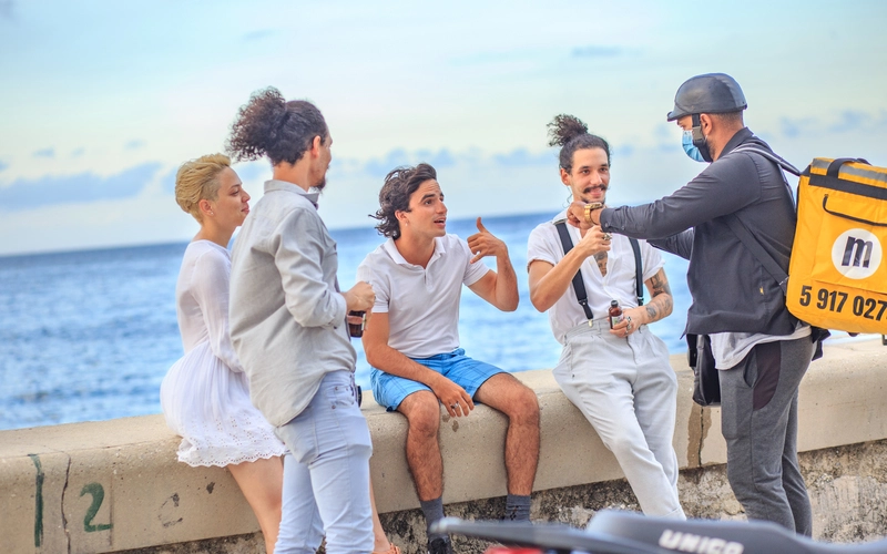 Amigos jÃ³venes beben cocteles cubanos a domicilio en el malecÃ³n de La Habana mientras conversan con un mandadero de Mandao