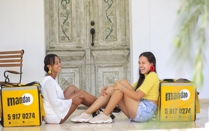 Mujeres cubanas jÃ³venes sonriendo con las mochilas del servicio de delivery de Mandao, en La Habana, Cuba