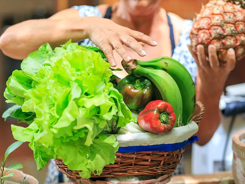 Vegetales y frutas siendo organizados en una cesta.